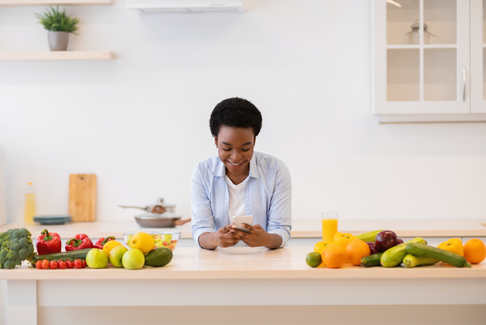 Black Lady Using Cellphone With Weight-Loss App Cooking In Kitchen