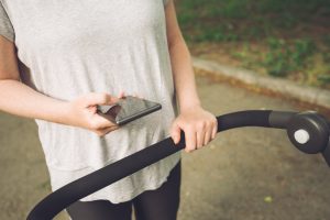 Mother pushing baby stroller and reading text message on smartph