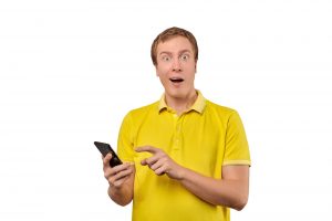 Surprised young man with smartphone, funny guy holding phone isolated on white background